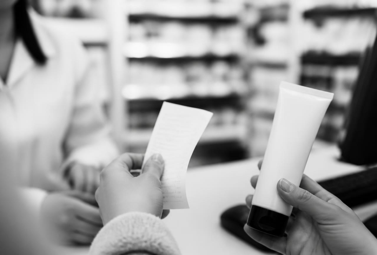 Shopper holding a receipt next to a skincare tube at the pharmacy checkout